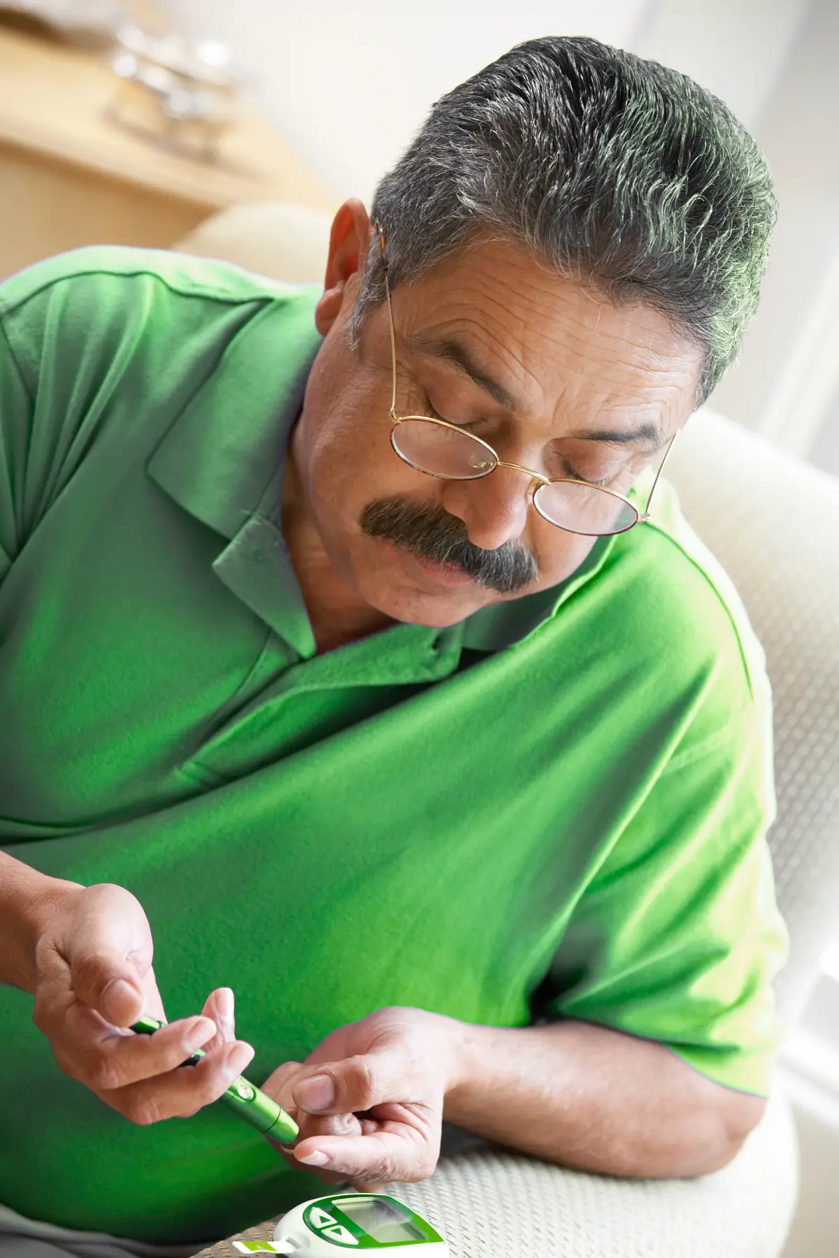 Middle-aged Hispanic man in green shirt drawing blood from finger for type 2 diabetes insulin test