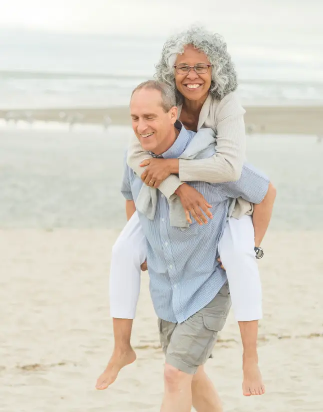 Older mixed-race couple riding piggyback on beach