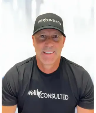 Headshot of Dr. John Friedrichs, owner of WellConsulted, wearing matching black WellConsulted baseball hat and t-shirt against white background