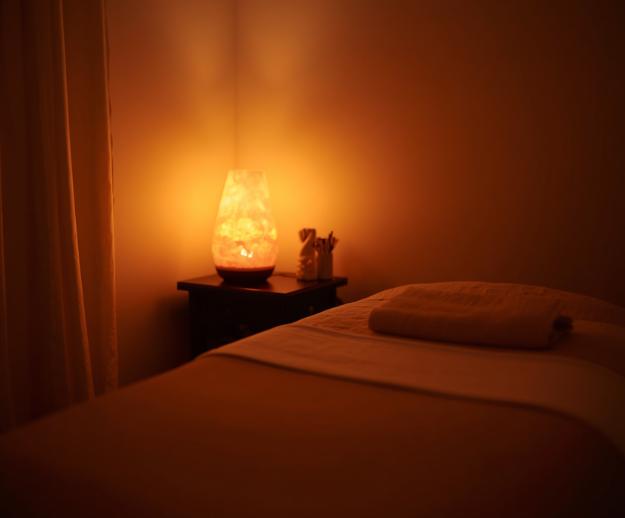 Dimly lit room with freshly made massage table and glowing orange salt lamp